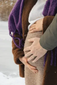 a pregnant woman is holding her belly in the snow
