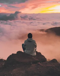 man sitting on cliff - signifying meditation