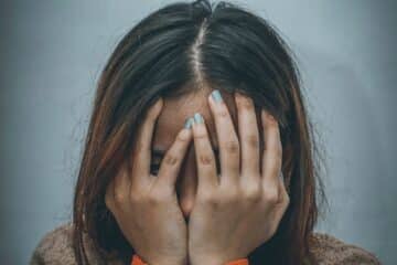 woman in brown sweater covering her face with her hand